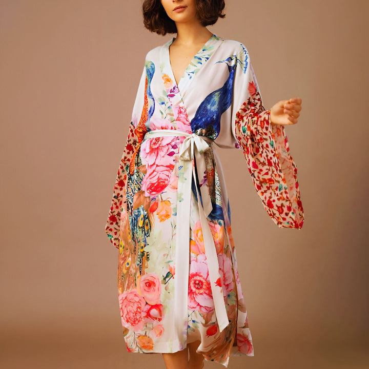 Femme portant un kimono en soie blanche avec des motifs de paons et de fleurs colorées. Vêtement d'intérieur élégant, parfait pour la détente ou comme peignoir original. Collection de kimonos de luxe.