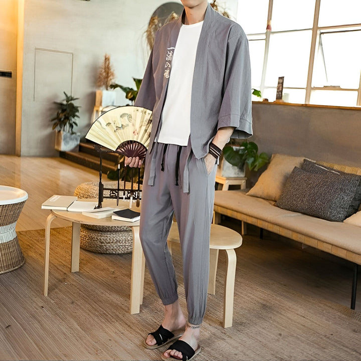 Homme portant un kimono gris décontracté avec un t-shirt blanc et un pantalon assorti. Il tient un éventail. Vêtements de style japonais pour hommes. Kimonos modernes et confortables à vendre.