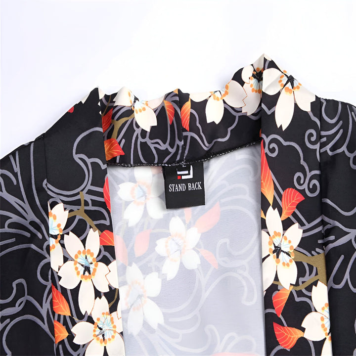 Détail d'un kimono avec des motifs de fleurs de cerisier blanches et feuilles orange sur fond noir. Etiquette "STAND BACK". Vêtement japonais traditionnel.