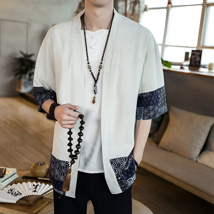 Homme portant un kimono beige à manches courtes avec motifs bleus, collier de perles et bracelet en bois. Vente de kimonos en ligne.
