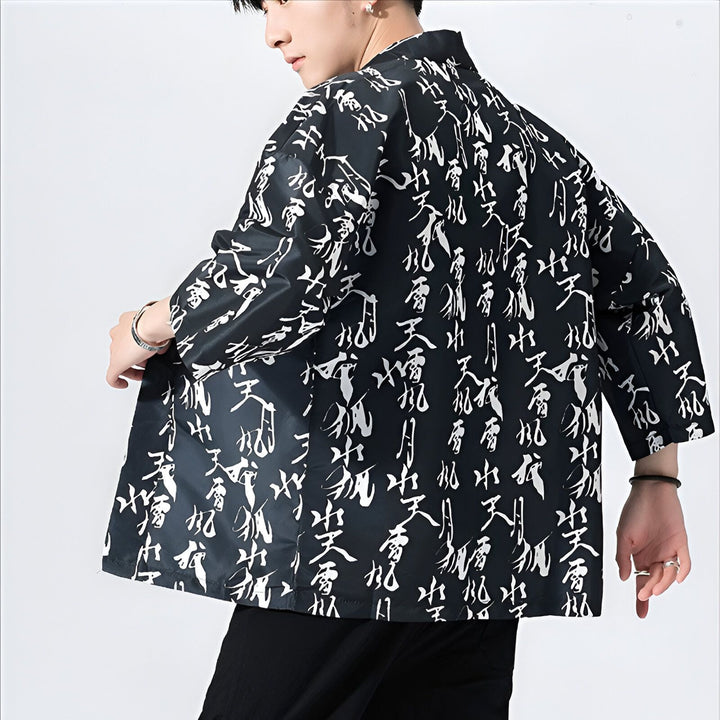 Homme portant un kimono noir imprimé de calligraphie blanche. Vêtement de style japonais, idéal pour un look tendance et unique. Découvrez notre collection de kimonos pour hommes.