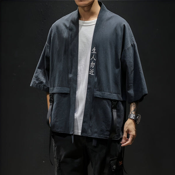 Homme portant un kimono gris anthracite avec inscription verticale blanche. Vêtement de style japonais avec poches et lanières. Collection de kimonos pour homme.