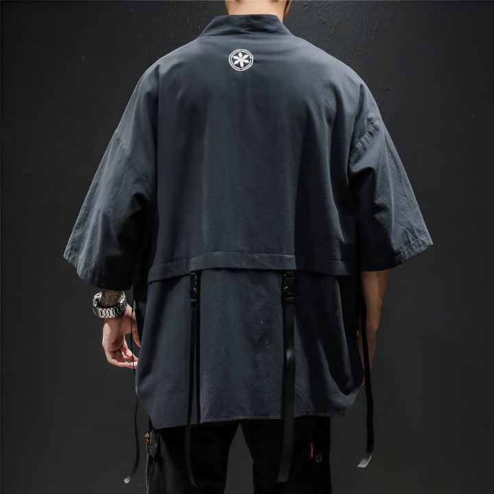 Dos d'un homme portant un kimono noir avec un motif floral blanc. Kimono à manches larges et lanières décoratives. Découvrez notre collection de kimonos uniques!