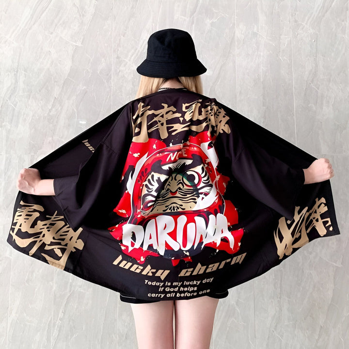 Kimono noir avec motif Daruma rouge et calligraphie dorée. Vêtement de style japonais. Idéal pour un look unique et tendance. Découvrez notre collection de kimonos.