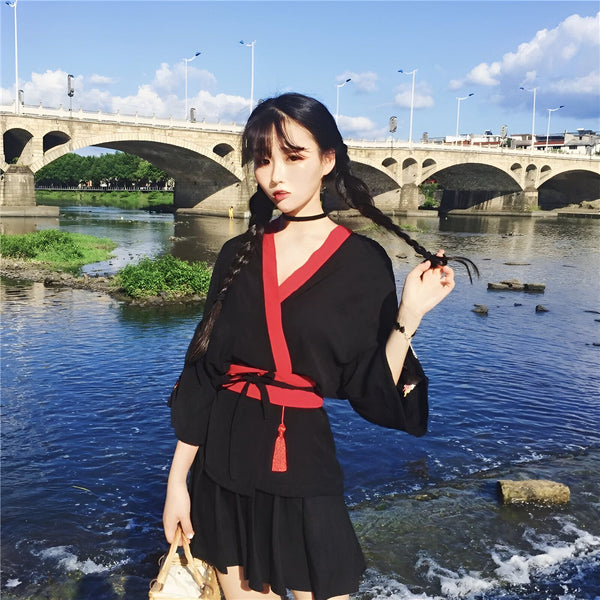 Jeune femme portant un kimono noir et rouge près d'une rivière avec un pont en arrière-plan. Vêtements de style japonais. Kimonos traditionnels et modernes à vendre.