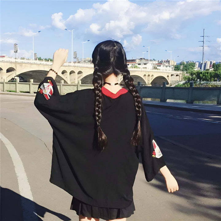 Femme portant un kimono noir brodé, vue de dos. Tresses longues. Style japonais moderne. Vêtements kimono uniques à découvrir.