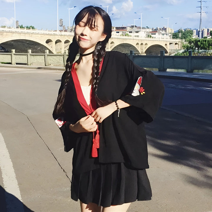 Jeune femme souriante portant un kimono noir avec des détails rouges et une broderie renard. Kimono ample, style japonais, avec des tresses. Vente de kimonos en ligne.