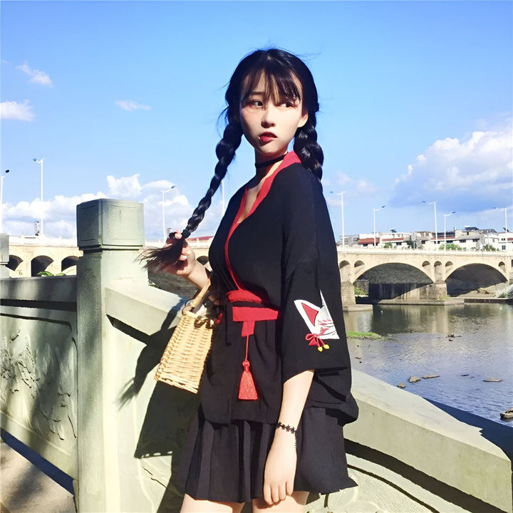 Jeune femme en kimono noir avec motif de renard rouge et blanc, tenant un sac en paille. Vente de kimonos en ligne.