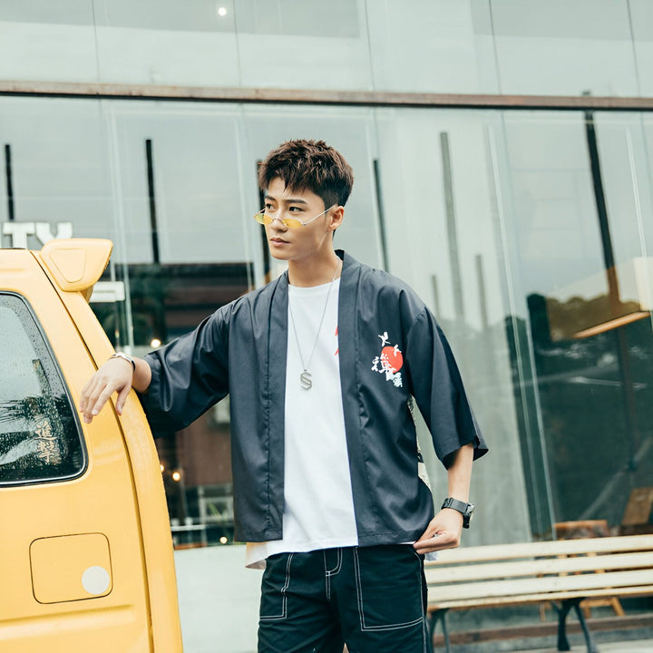 Homme portant un kimono noir avec motif japonais, appuyé contre une voiture jaune. Vente de kimonos pour hommes et femmes. Mode asiatique moderne.