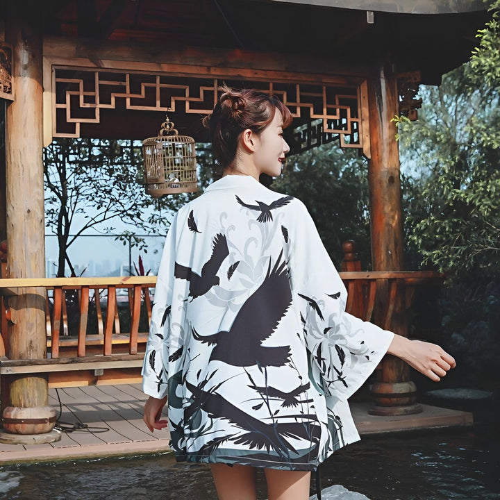 Femme portant un kimono blanc à motifs d'oiseaux noirs devant un pavillon asiatique. Vêtements traditionnels japonais à la vente.