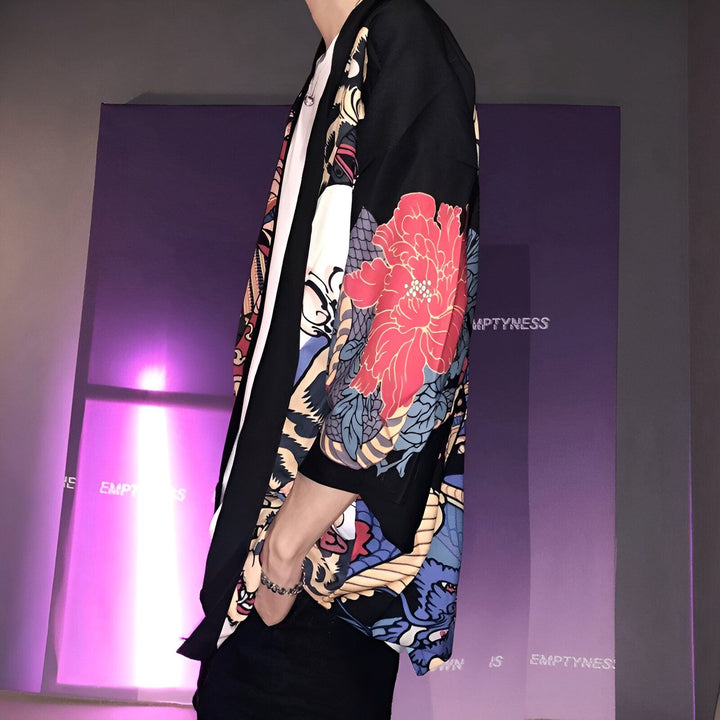 Homme portant un kimono noir orné de motifs floraux rouges et bleus. Vêtement de style japonais, idéal pour une tenue décontractée et tendance. Découvrez notre collection de kimonos uniques.