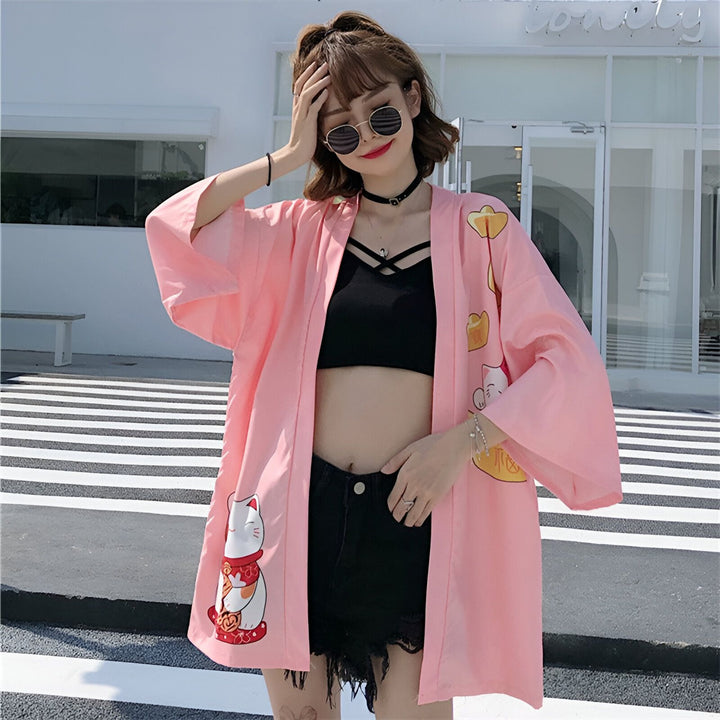 Femme portant un kimono rose avec motifs de chats Maneki Neko. Kimono tendance pour un look décontracté et stylé. Découvrez notre collection de kimonos uniques.