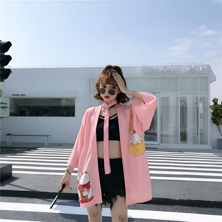 Femme portant un kimono rose avec motifs de chat Maneki Neko. Vêtements japonais modernes. Kimono pour femmes, style décontracté. Mode asiatique. Boutique de kimonos en ligne.