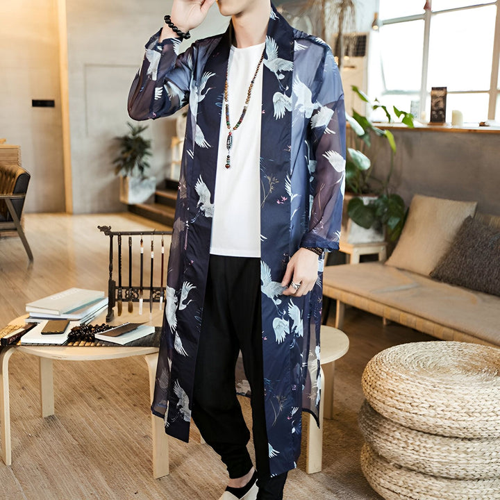 Homme portant un kimono long bleu marine avec motifs de grues blanches. Vêtement de style japonais, idéal pour compléter une garde-robe élégante et décontractée. Kimonos à motifs originaux en vente.