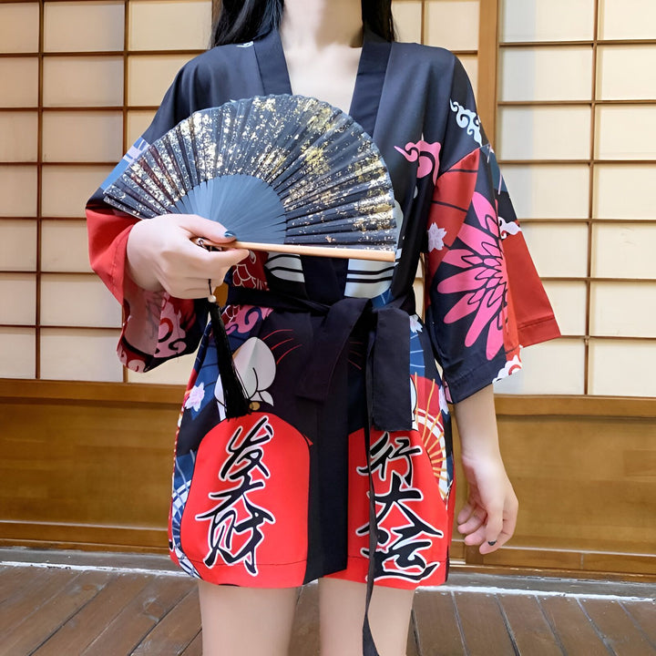 Femme portant un kimono japonais traditionnel noir et rouge avec des motifs floraux et des lanternes, tenant un éventail décoratif noir et or. Vêtements japonais authentiques, vente de kimonos.