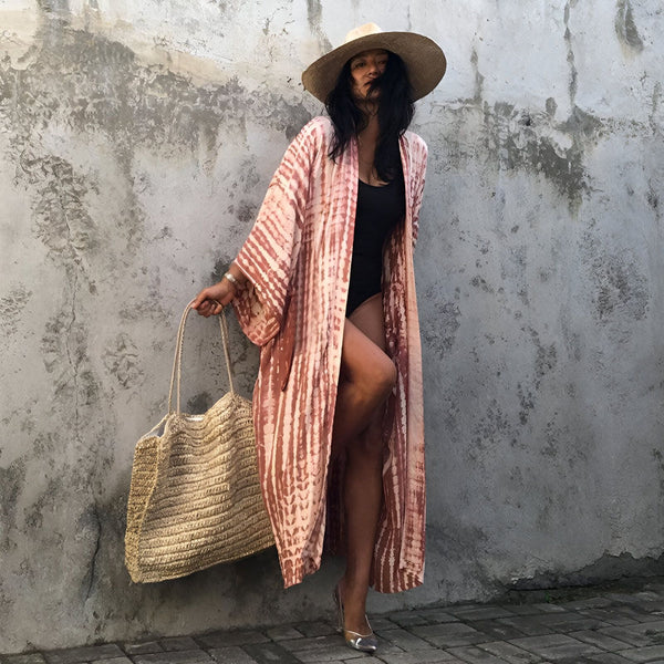 Femme portant un kimono long à rayures roses et marron, un maillot de bain noir, un chapeau de paille et tenant un sac de plage. Vêtements d'été, style bohème. Kimonos tendance.