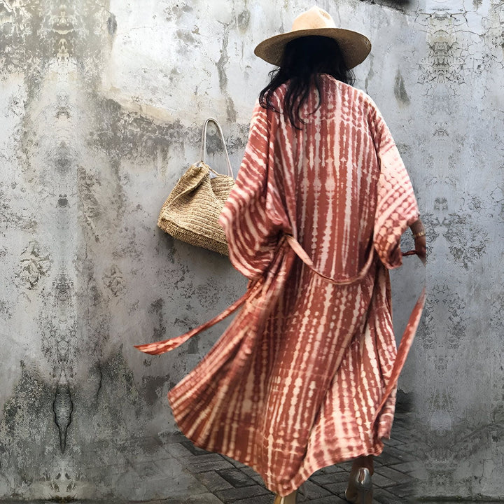 Femme portant un kimono tie-dye marron et blanc, vue de dos. Chapeau de paille et sac en fibres naturelles. Collection de kimonos chics et confortables.