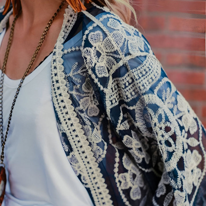 Kimono bleu marine en dentelle blanche porté par une femme, détail du motif floral et de la bordure délicate. Vêtement d'extérieur tendance.