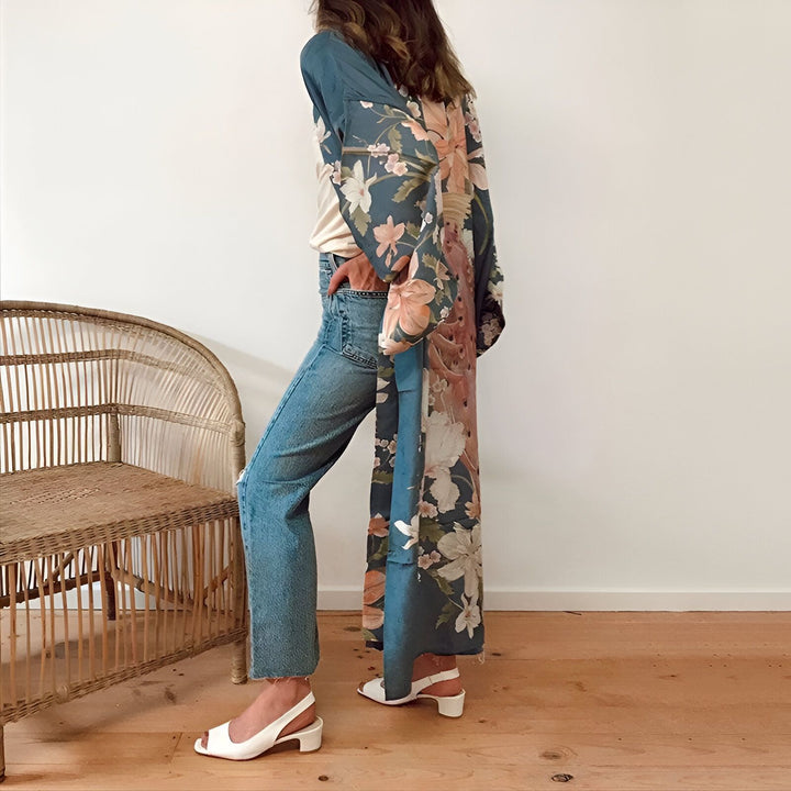 Femme portant un kimono long à motifs floraux bleus et roses, avec un jean bleu et des chaussures blanches. Vente de kimonos en ligne.