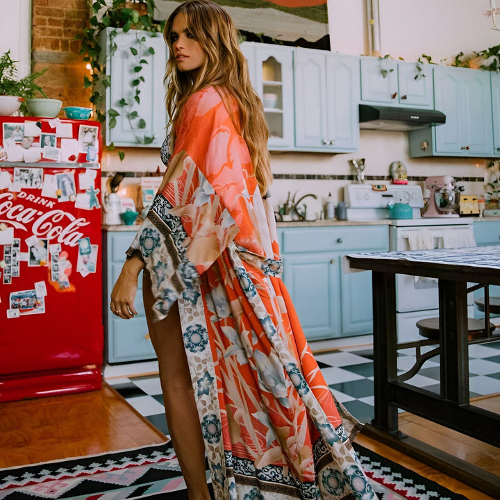 Femme portant un kimono fleuri orange dans une cuisine vintage. Kimono à motifs floraux disponible à l'achat.