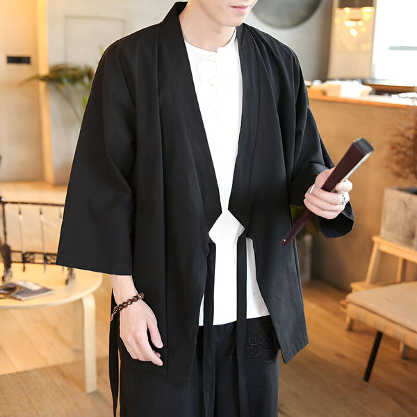 Homme portant un kimono noir traditionnel avec une chemise blanche et un pantalon noir. Détails : large col, manches amples, ceinture nouée. Style japonais décontracté et élégant.
