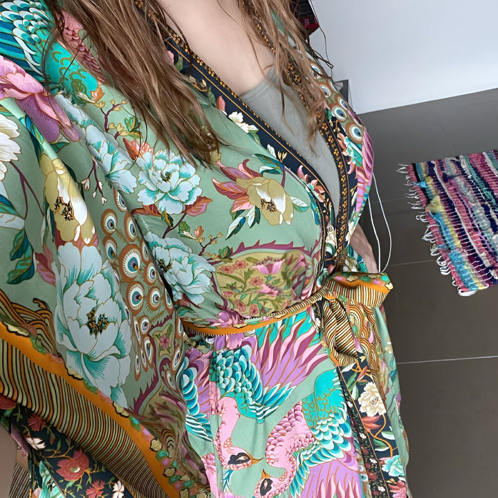 Femme portant un kimono fleuri coloré. Kimono long vert avec motifs floraux et oiseaux, ceinture nouée à la taille. Mode kimono, style bohème, vente de kimonos en ligne.