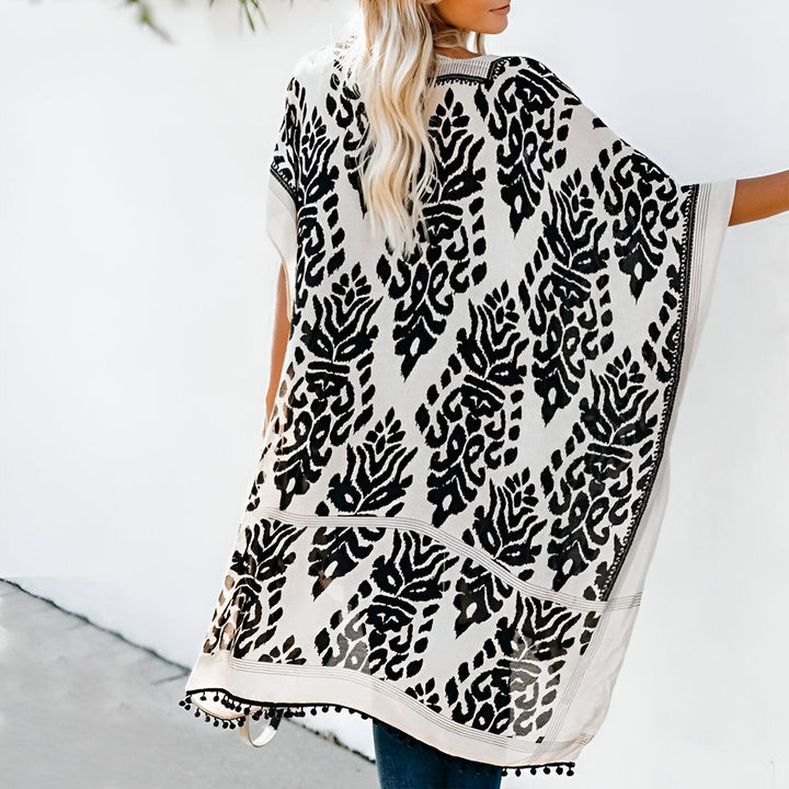 Kimono femme blanc à motifs noirs. Vêtement léger, idéal pour l'été. Détails de pompons noirs en bas. Style bohème chic. Découvrez notre collection de kimonos tendance.