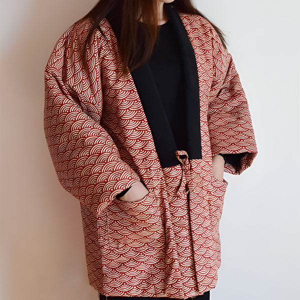 Kimono rouge avec motif vague, col noir et poches, porté par une femme. Vêtement japonais traditionnel et élégant.
