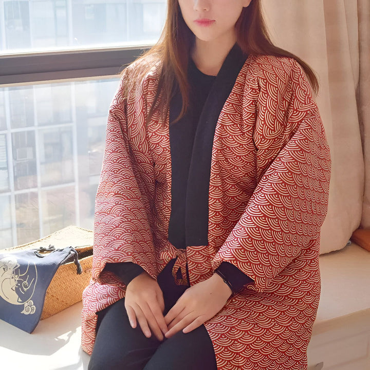 Femme portant un kimono rouge à motifs japonais, assise près d'une fenêtre. Kimonos de qualité pour un style unique. Découvrez notre collection de kimonos traditionnels et modernes.
