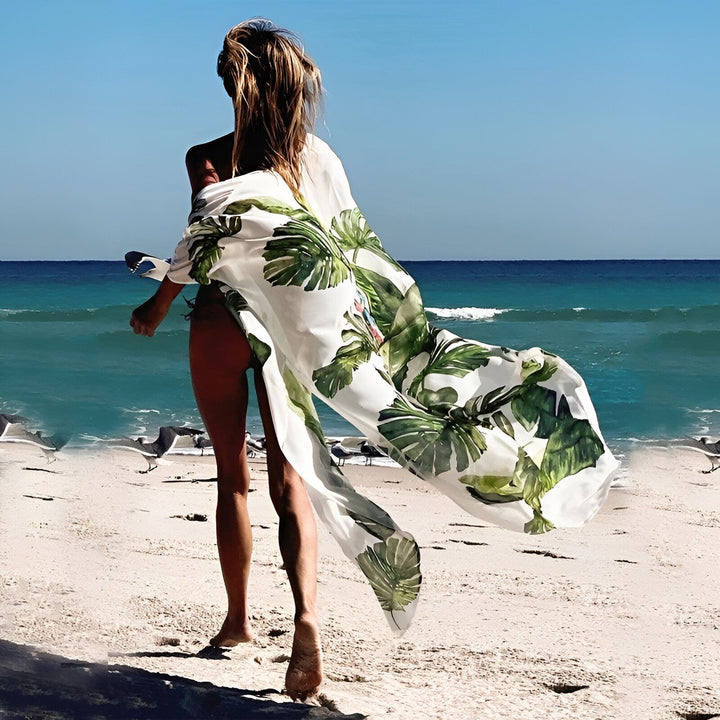 Femme de dos portant un kimono imprimé feuilles de palmier sur la plage. Kimonos de plage tendance.
