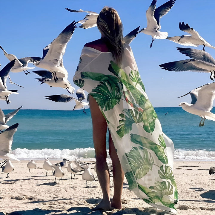 Femme sur la plage portant un kimono à motifs de feuilles tropicales, entourée de mouettes. Kimonos légers parfaits pour l'été.