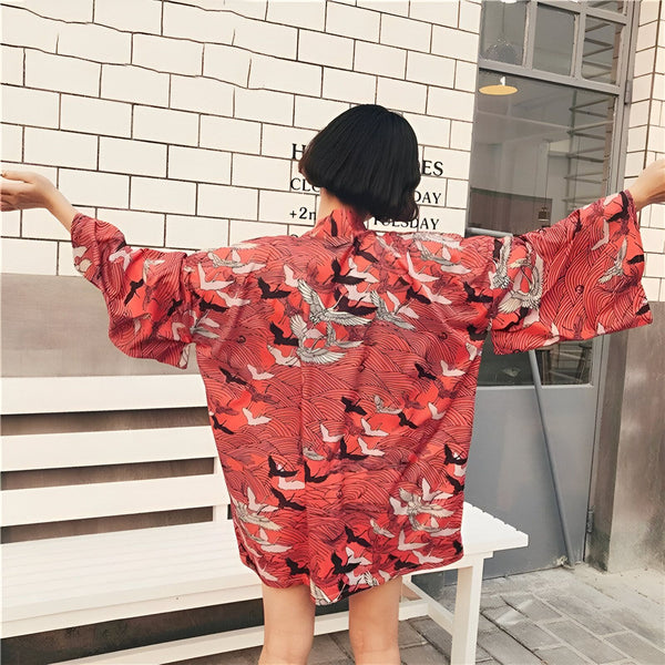 Femme portant un kimono rouge à motifs de grues. Vêtement de style japonais avec des manches larges. Kimonos uniques à acheter en ligne. Mode asiatique.