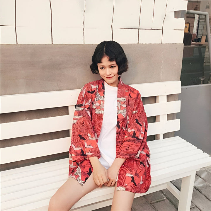 Femme assise portant un kimono rouge imprimé de grues. Kimono traditionnel japonais. Boutique de kimonos en ligne.