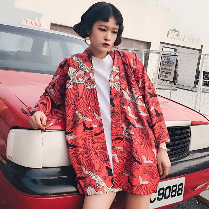 Femme portant un kimono rouge imprimé avec des grues blanches. Vêtements japonais traditionnels revisités. Découvrez notre collection de kimonos pour femmes.