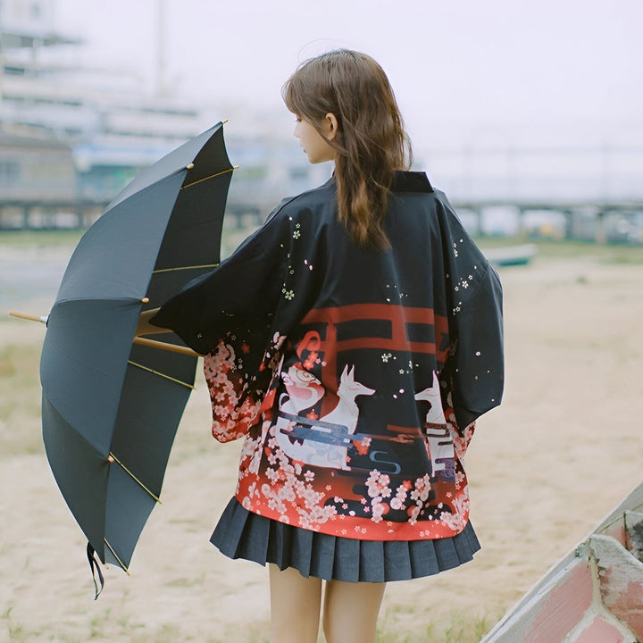 Femme portant un kimono japonais noir à motifs floraux et de renards, tenant un parapluie. Vente de kimonos traditionnels et modernes. Découvrez notre collection unique !