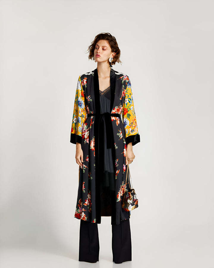 Femme portant un kimono long fleuri avec une ceinture noire en velours. Kimono noir avec des motifs floraux colorés et manches jaunes. Vêtements de détente élégants à vendre.