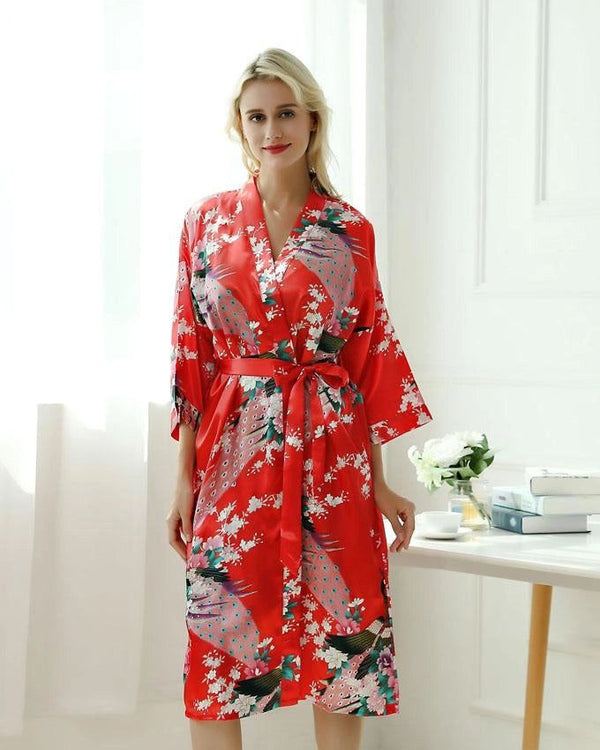 Femme portant un kimono rouge à motifs floraux et de paon. Kimono avec ceinture assortie. Parfait pour se détendre avec style. Découvrez notre collection de kimonos.