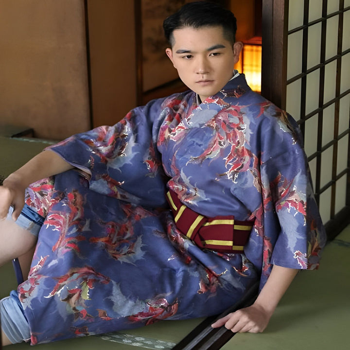 Homme en kimono bleu à motifs floraux rouges, assis sur un tatami. Ceinture obi bordeaux et or. Vêtements traditionnels japonais. Kimonos de qualité à vendre en ligne.