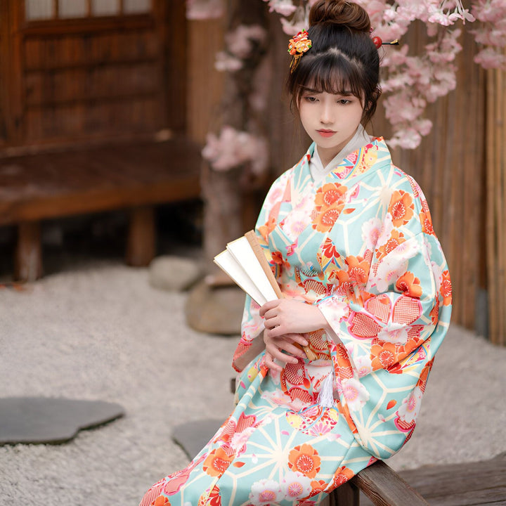 Femme portant un kimono traditionnel japonais turquoise avec motifs floraux oranges. Elle tient un éventail. Vêtements japonais authentiques.