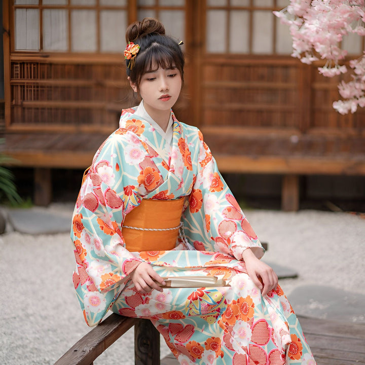 Femme portant un kimono fleuri bleu et orange. Vente de kimonos traditionnels japonais. Tenue élégante pour occasions spéciales. Mode japonaise authentique.
