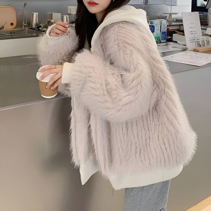 Femme portant un manteau kimono en fausse fourrure beige clair avec capuche blanche, tenant une tasse de café. Vêtements d'hiver tendance.