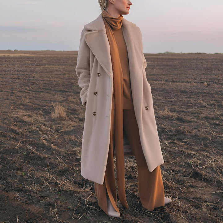 Femme portant un manteau long beige sur un ensemble marron dans un champ. Idée de tenue inspirée du style kimono.