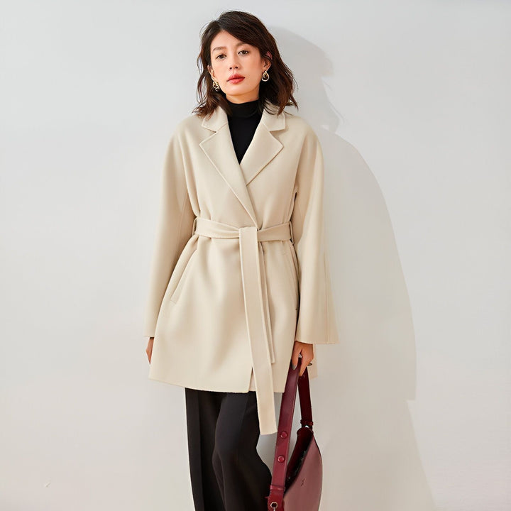 Femme portant un kimono beige noué à la taille, col roulé noir, pantalon noir. Sac à main bordeaux. Kimono élégant et moderne. Collection kimono.