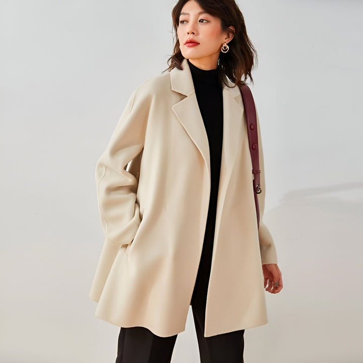 Femme portant un kimono beige ouvert sur un col roulé noir. Sac à bandoulière bordeaux. Vêtements style kimono disponibles à l'achat.