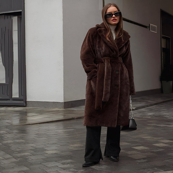 Femme portant un long manteau en fausse fourrure marron, style kimono. Look élégant avec des lunettes de soleil noires et un col roulé blanc. Vêtements d'extérieur tendance, idéal pour l'hiver.
