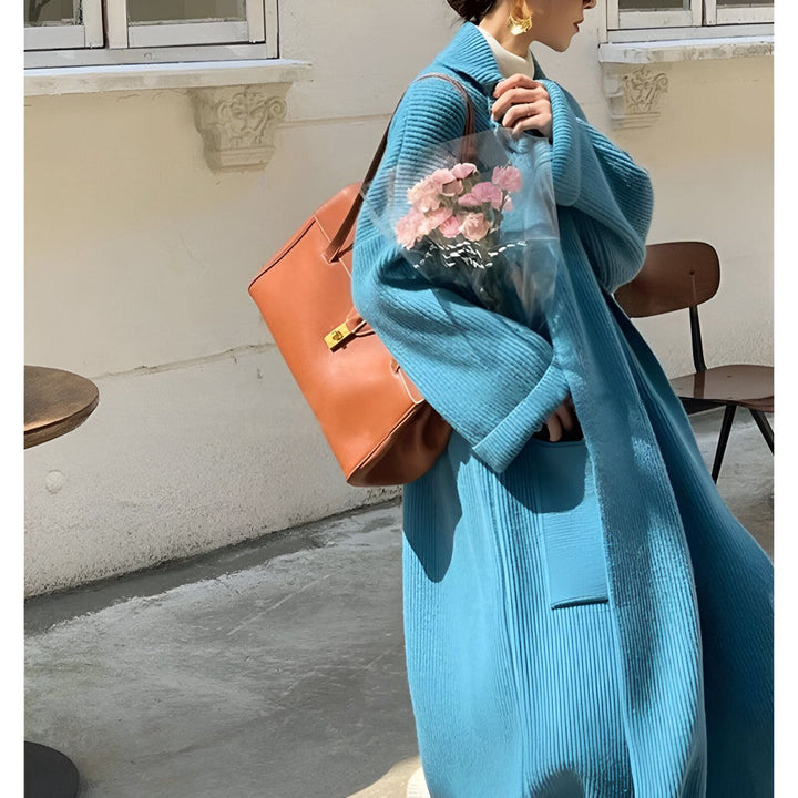 Femme portant un kimono bleu texturé, sac en cuir marron et fleurs roses. Vêtements de style kimono.
