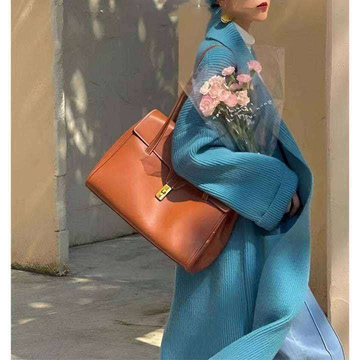 Femme portant un kimono bleu turquoise avec un sac à main en cuir marron et des fleurs roses. Découvrez notre collection de kimonos uniques.