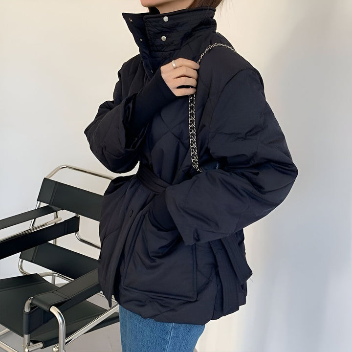 Veste kimono matelassée noire pour femme avec ceinture et col montant, présentée avec un sac à chaîne. Mode kimono moderne et élégante.