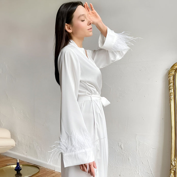 Femme portant un kimono blanc élégant avec des plumes aux manches. Kimono de notre collection, idéal pour se détendre avec style. Découvrez nos kimonos de luxe.
