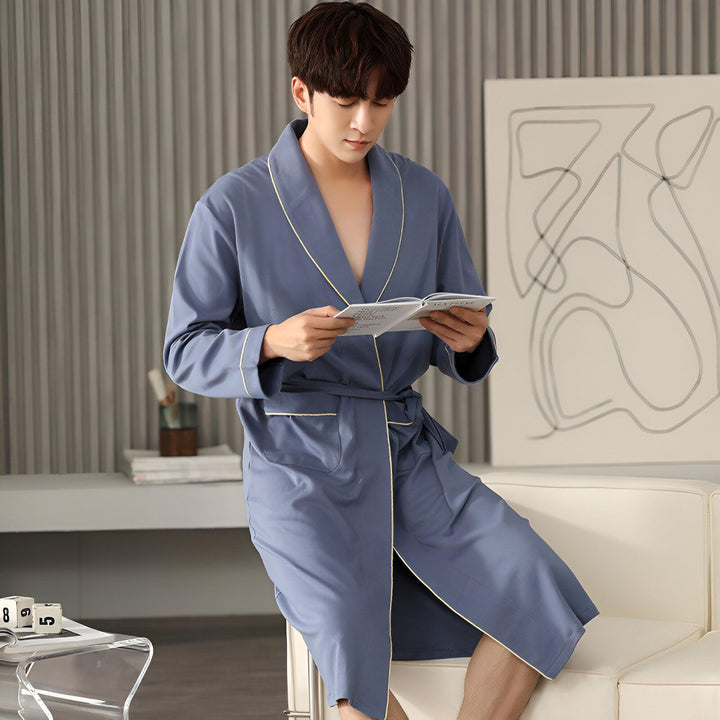 Homme asiatique en kimono bleu lisant. Vente de kimonos en ligne. Confort et style japonais. Découvrez notre collection de kimonos pour hommes.